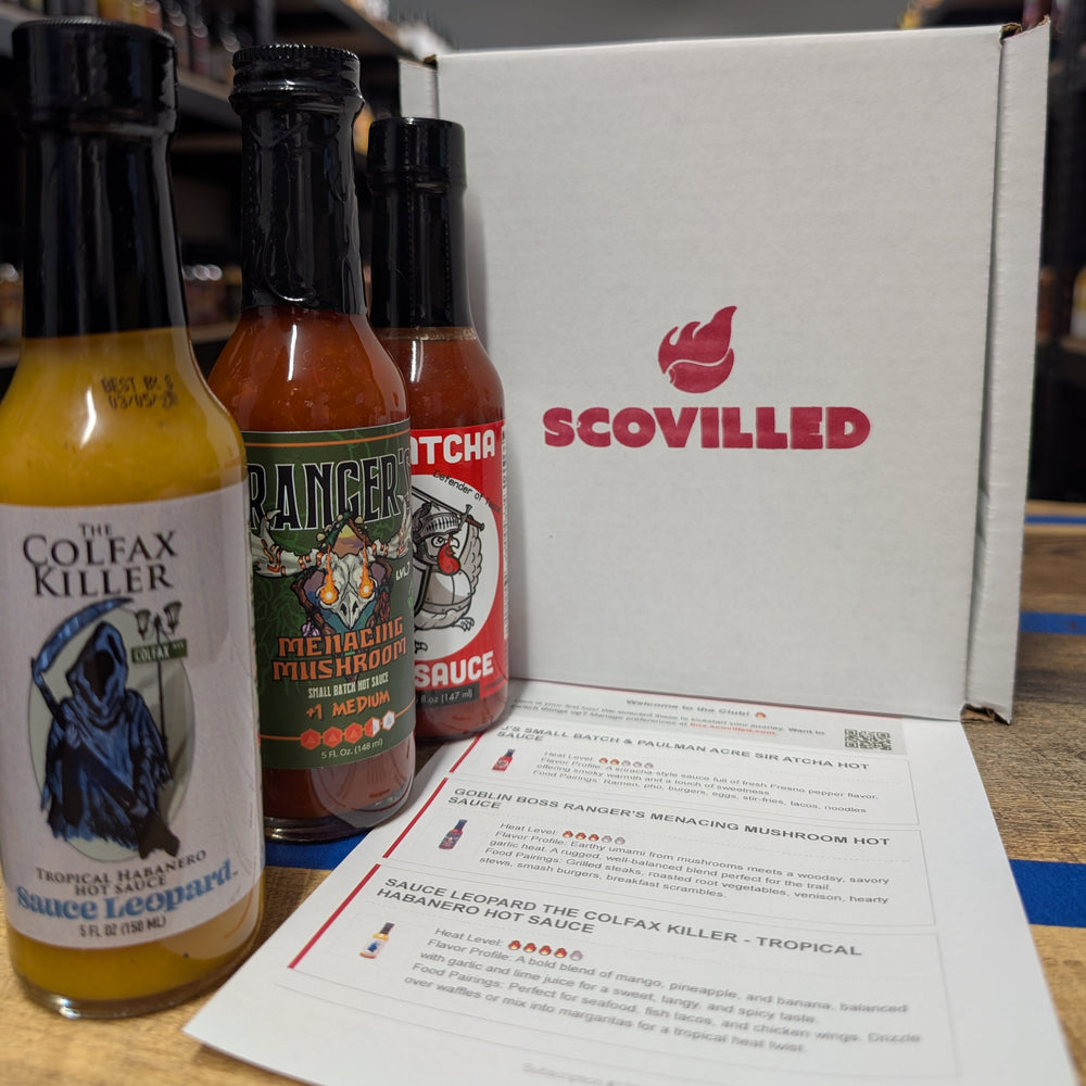 Open SCOVILLED hot sauce subscription box with three small-batch bottles beside a printed card listing each sauce's heat level and food pairings