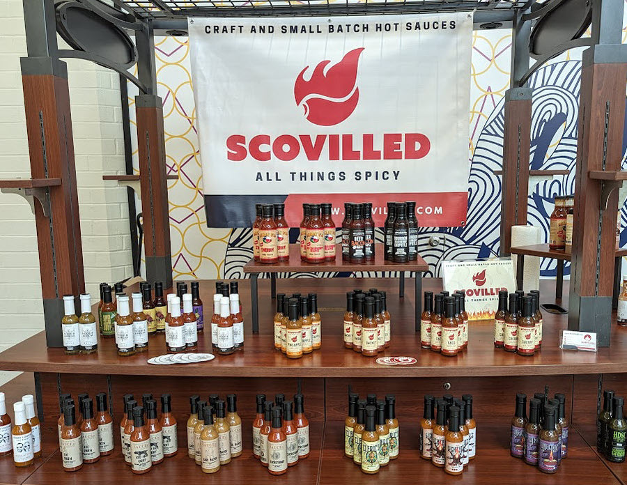 An early SCOVILLED pop-up stand with a branded banner and rows of craft hot sauce bottles