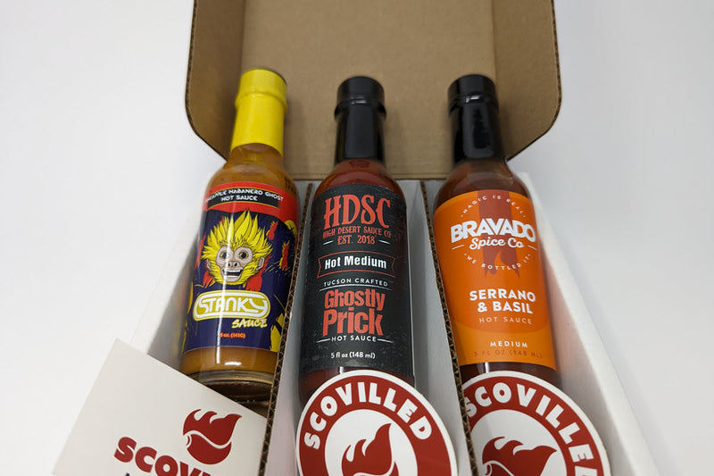 Open SCOVILLED subscription box packed with three pizza-friendly hot sauces: a pineapple habanero ghost sauce, High Desert Sauce Co. Ghostly Prick, and Bravado Spice Co. Serrano & Basil